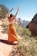 woman in orange dress standing on brown rock formation during daytime