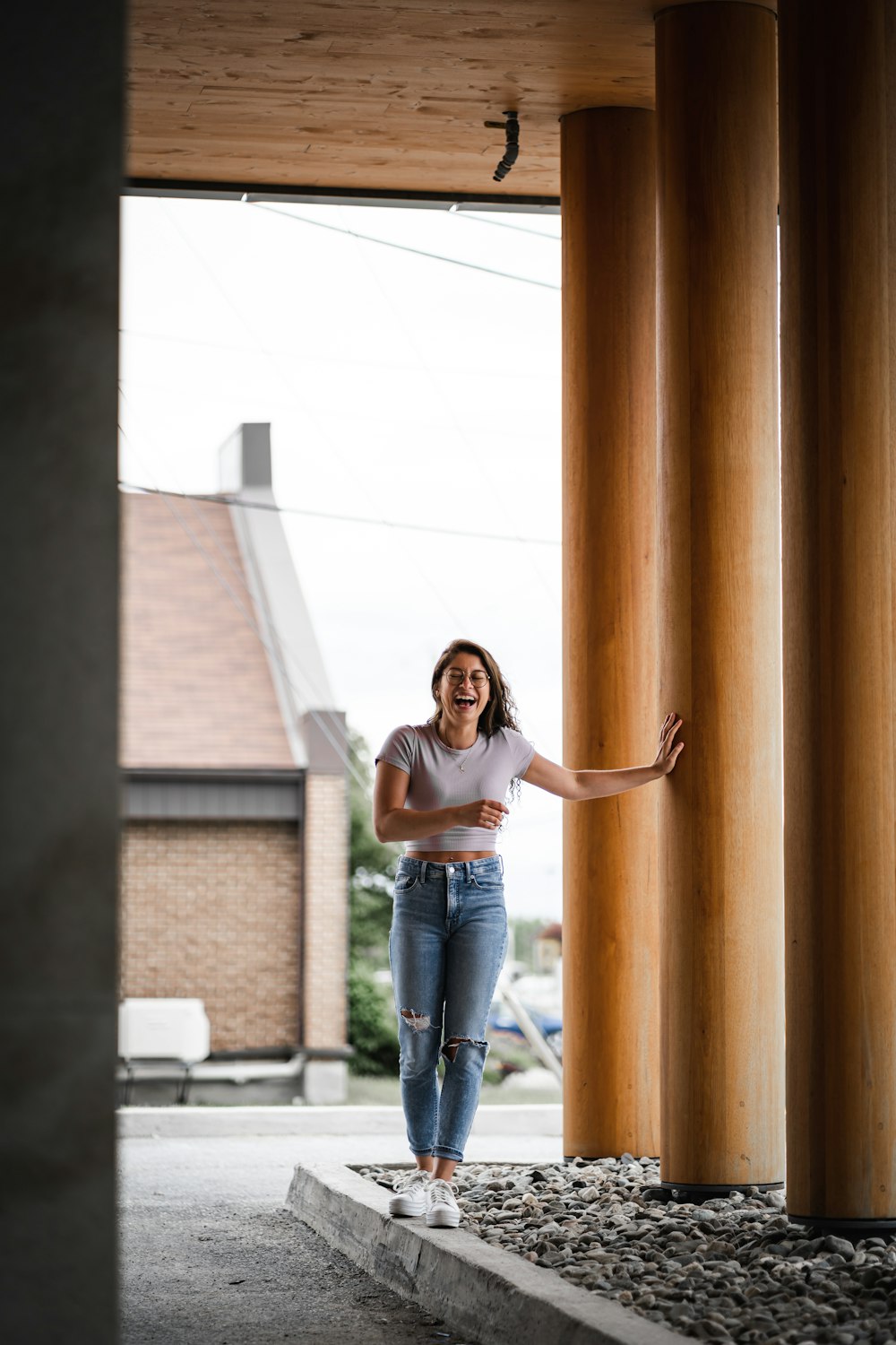 mulher na camisa branca e jeans azuis apoiando-se na parede de madeira marrom durante o dia