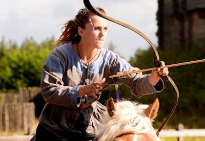 Mounted archer in action, drawing a bow while riding a horse across open terrain.
