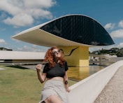 woman in black crop top and white and black striped skirt sitting on white concrete bench