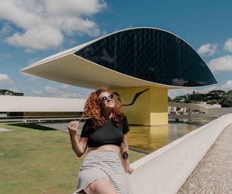 woman in black crop top and white and black striped skirt sitting on white concrete bench