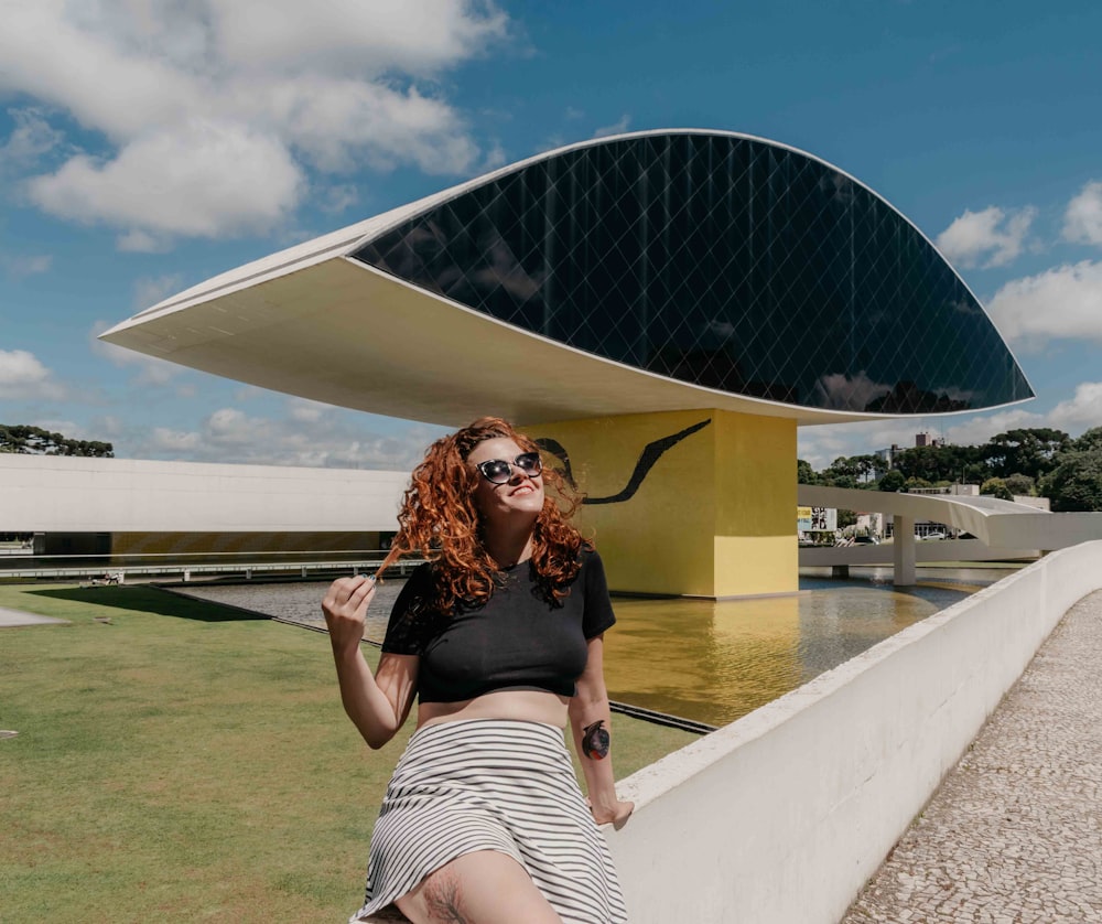 woman in black crop top and white and black striped skirt sitting on white concrete bench