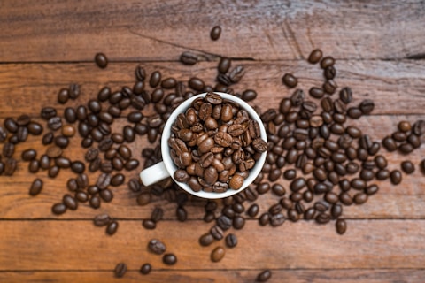 a cup filled with coffee beans on top of a wooden table