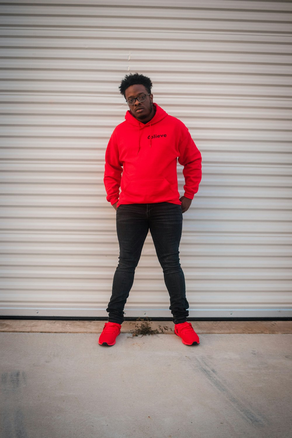 man in red hoodie standing beside white wall