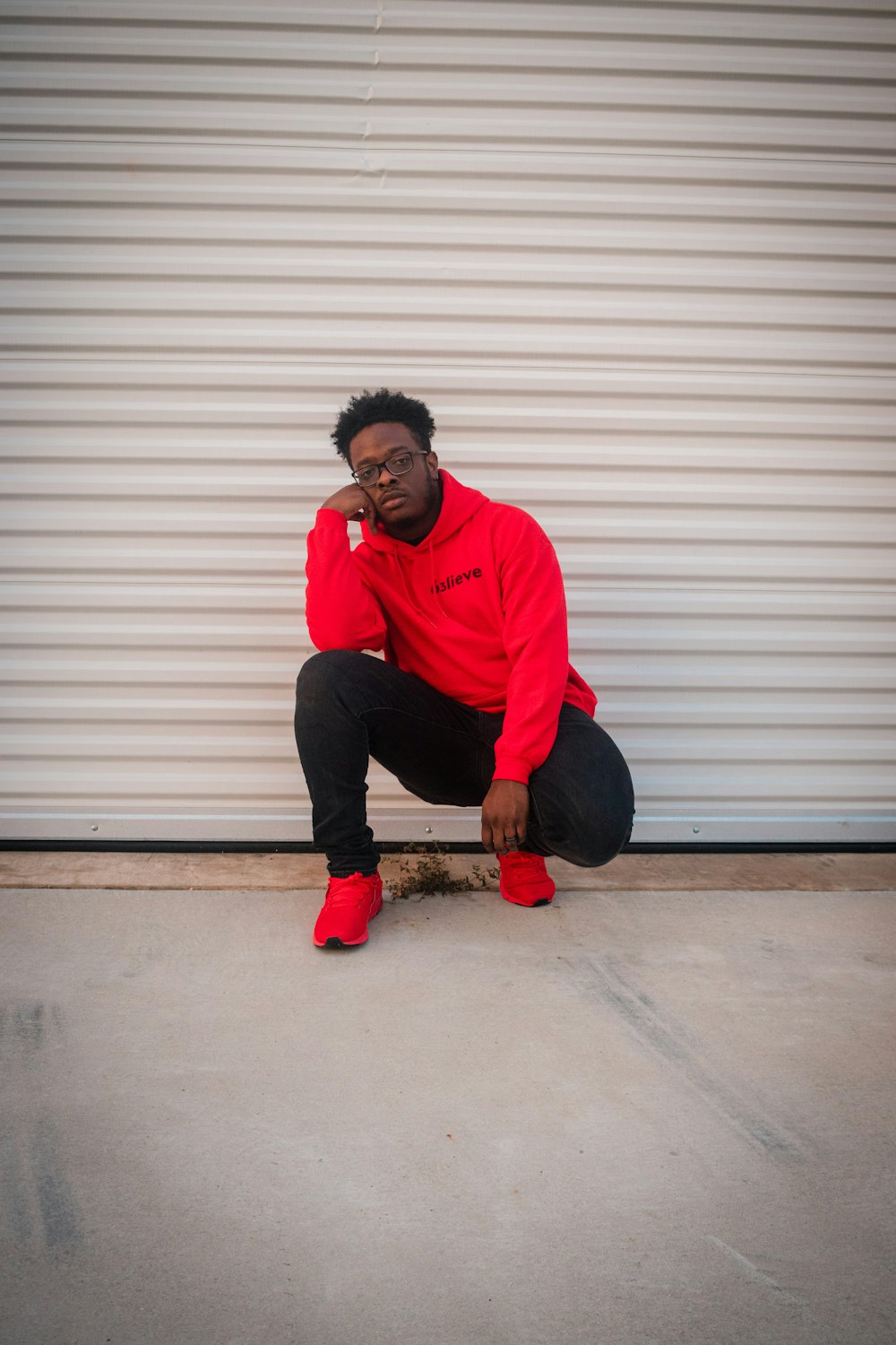 man in red sweater and blue denim jeans sitting on white roll up door