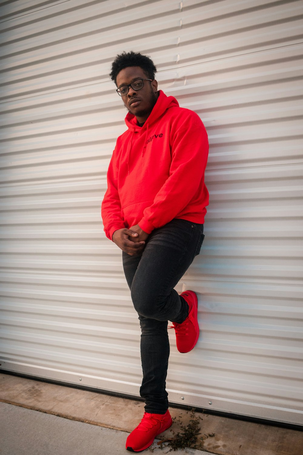 man in red dress shirt and black denim jeans standing beside white wall