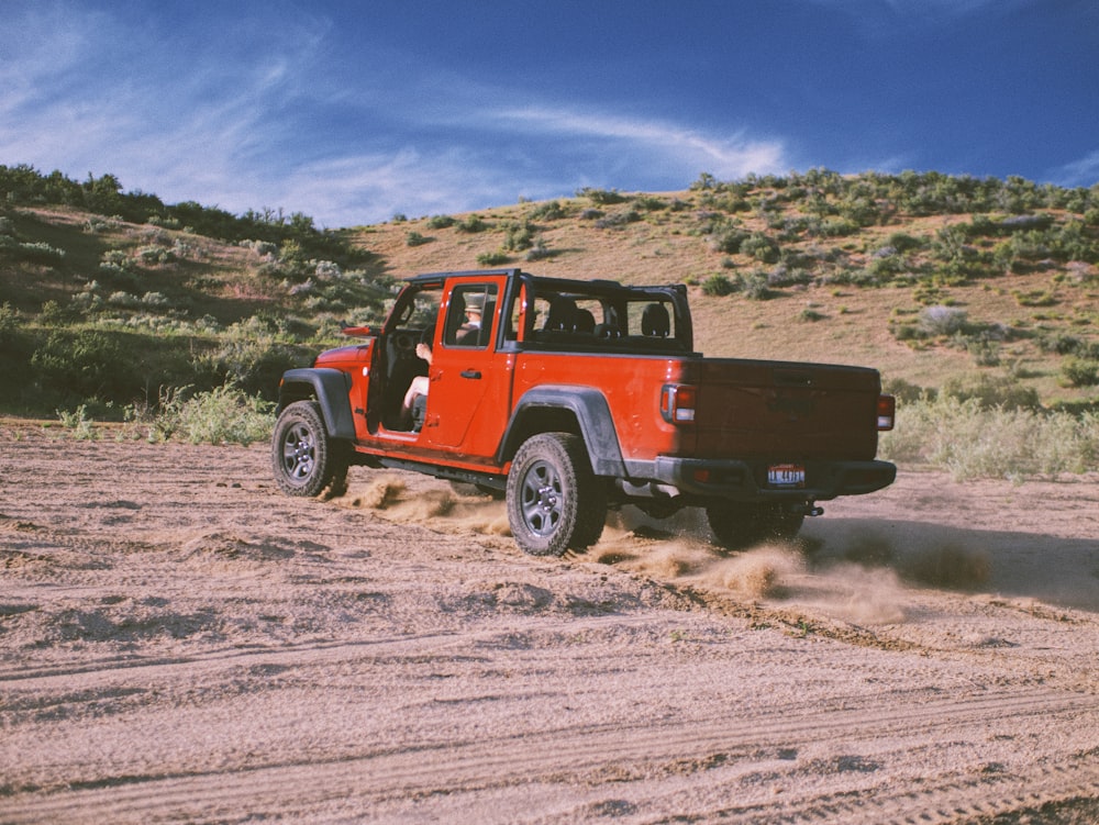 red and black jeep wrangler on brown field under blue and white cloudy sky during daytime
