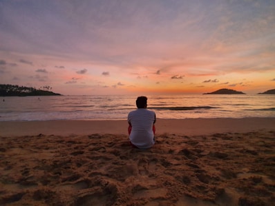 man in white shirt sitting on beach during sunset