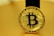A golden coin featuring the Bitcoin symbol in the center, surrounded by intricate circuit-like designs. The coin bears the words 'Bitcoin' and 'Blockchain Token', along with other related terminology. The background is also golden, harmonizing with the color of the coin.