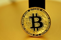 A golden coin featuring the Bitcoin symbol in the center, surrounded by intricate circuit-like designs. The coin bears the words 'Bitcoin' and 'Blockchain Token', along with other related terminology. The background is also golden, harmonizing with the color of the coin.
