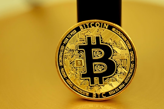 A golden coin featuring the Bitcoin symbol in the center, surrounded by intricate circuit-like designs. The coin bears the words 'Bitcoin' and 'Blockchain Token', along with other related terminology. The background is also golden, harmonizing with the color of the coin.