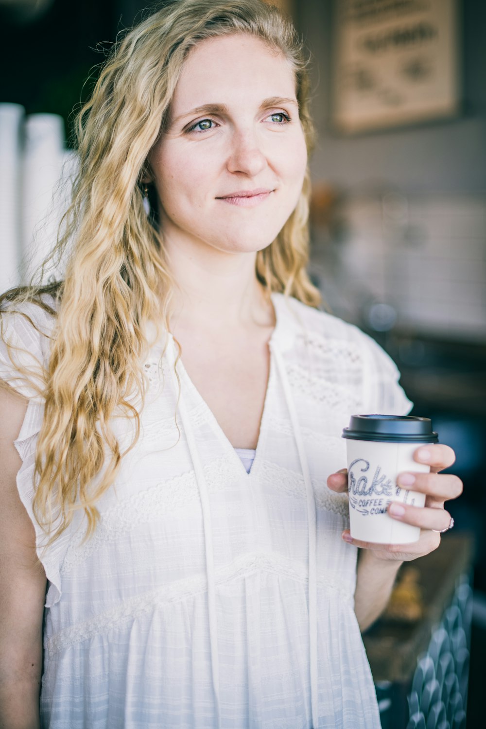 woman in white sleeveless dress holding white disposable cup