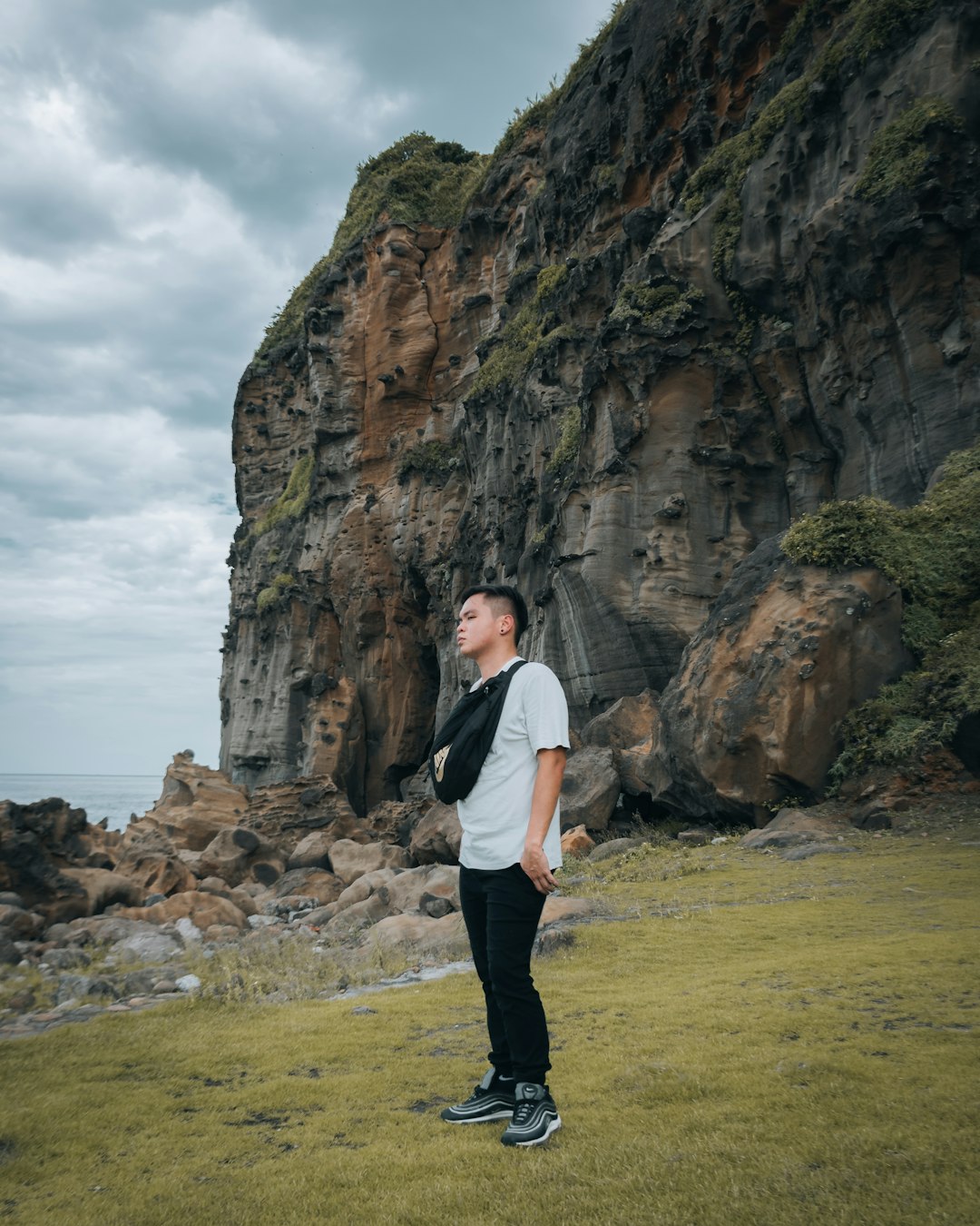 man in white dress shirt and black pants standing on green grass field near brown rocky