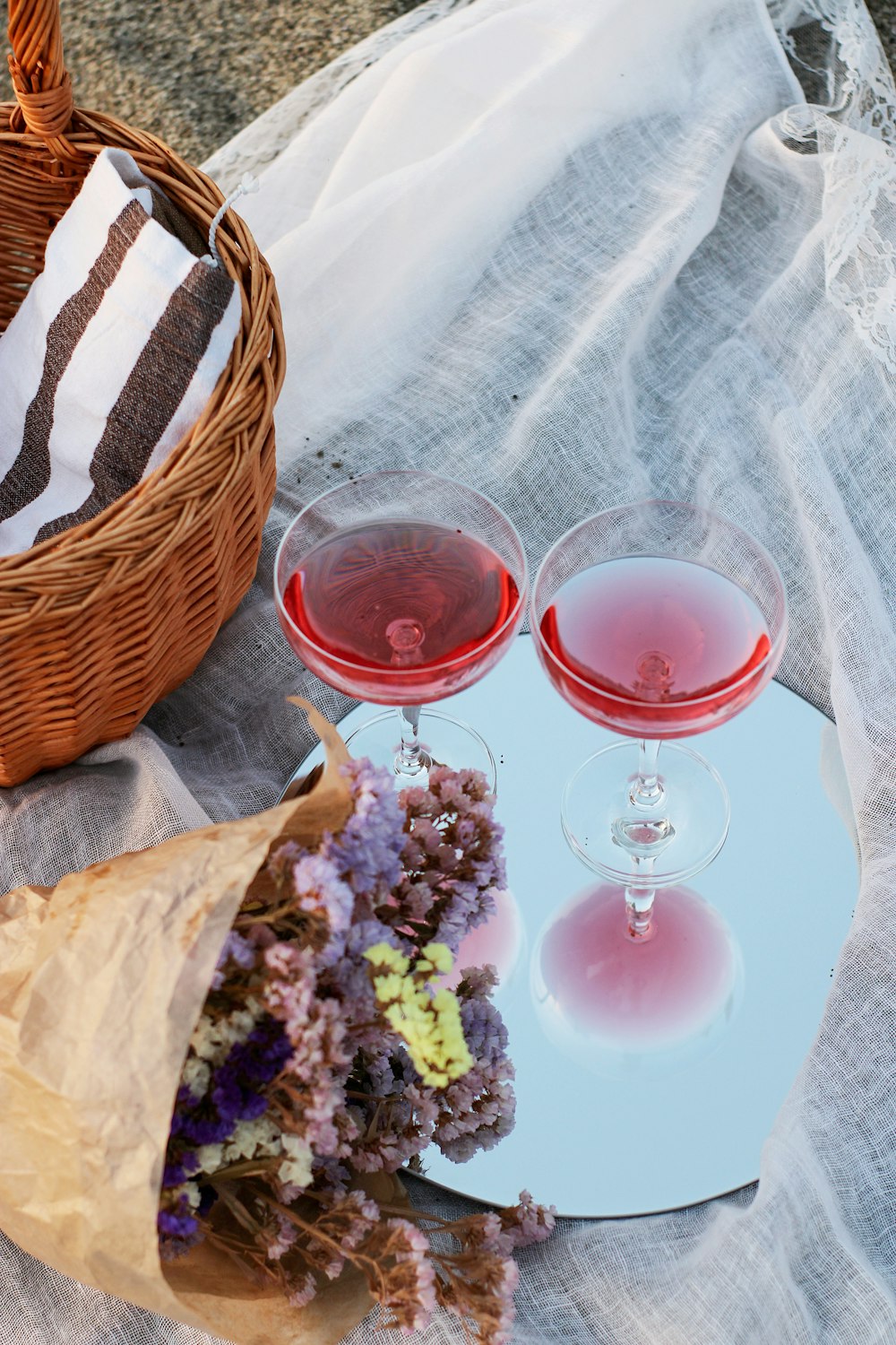 茶色の編まれたバスケットの横の赤と透明のワイングラス