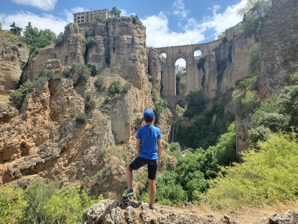 man in blue t-shirt and blue shorts walking on rocky hill during daytime