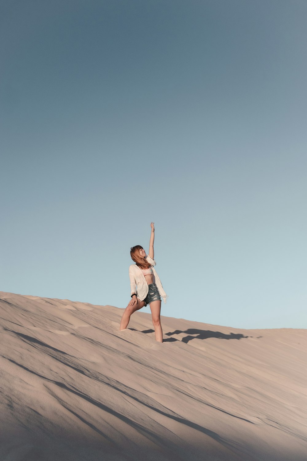 Frau in weißem Tanktop und blauen Jeansshorts, die tagsüber auf braunem Sand laufen