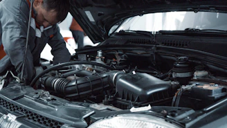 A mechanic in a grey uniform inspecting the engine of a car