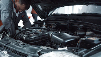 A mechanic in a grey uniform inspecting the engine of a car