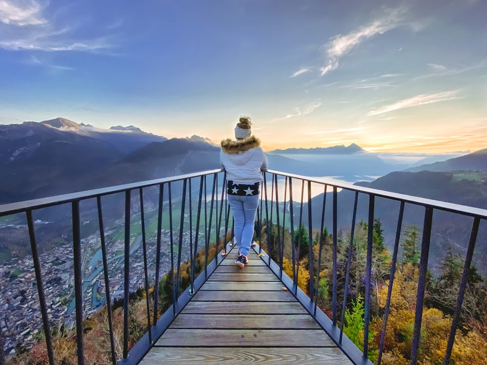 man in white hoodie standing on brown wooden bridge during daytime