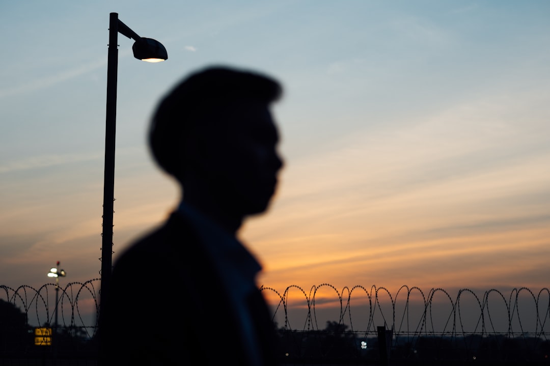 silhouette of man standing near light post during sunset