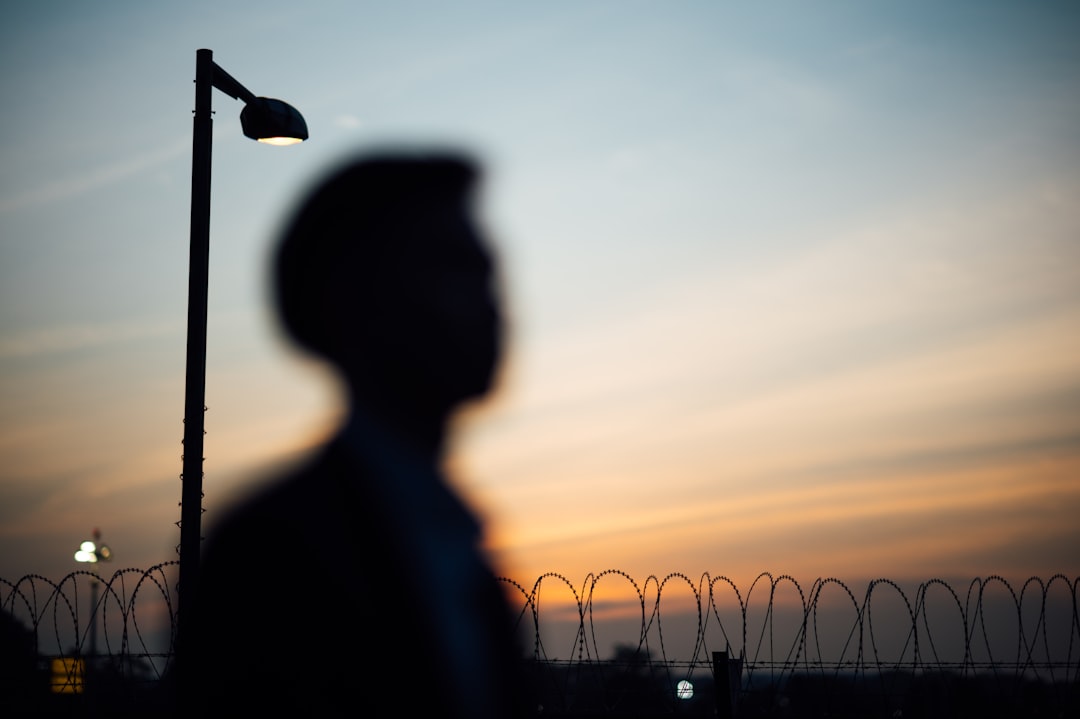 silhouette of man standing near fence during sunset