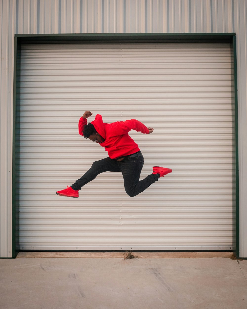 赤いパーカーを着た男が白いロールアップドアの前でジャンプ