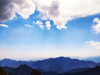 Serene mountain range under a soft blue sky with wispy white clouds.