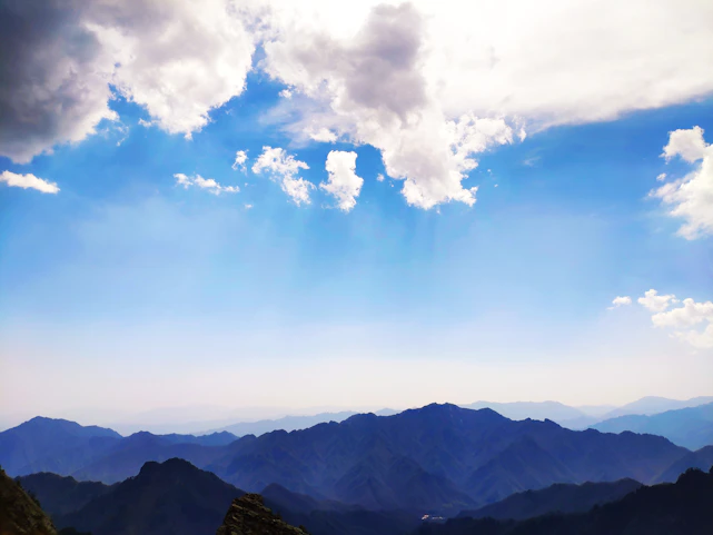 Serene mountain range under a soft blue sky with wispy white clouds.