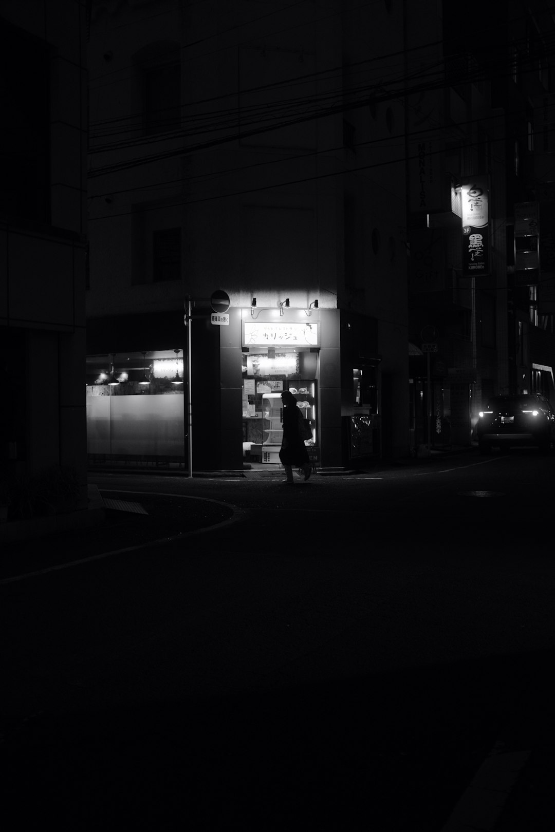 grayscale photo of person walking on sidewalk during night time