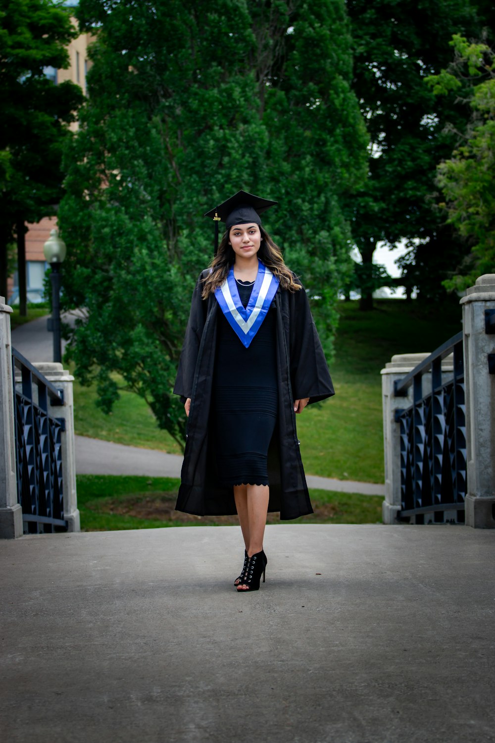 woman in black academic dress standing on gray concrete pathway during daytime