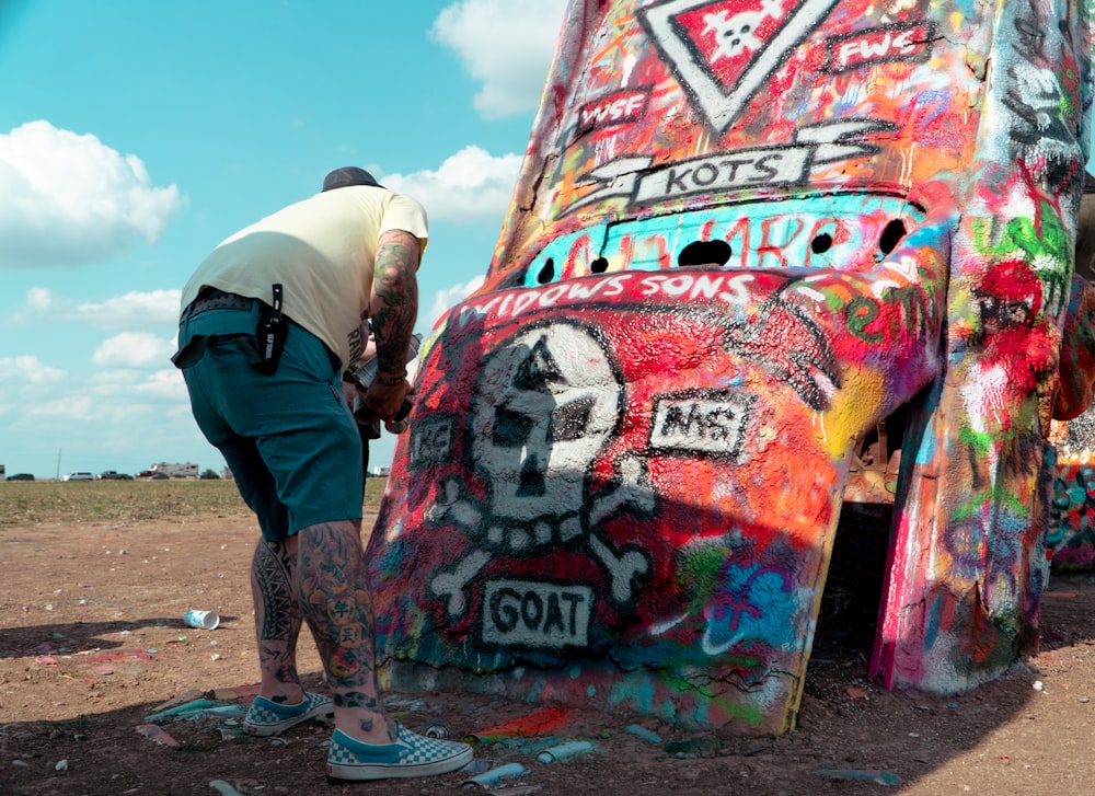 man in white t-shirt and black pants standing beside graffiti wall during daytime