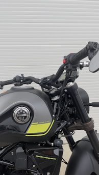 A close-up view of a motorcycle showcasing the handlebars and fuel tank. The motorcycle is designed with sleek black and gray colors, featuring the brand name 'Benelli' on the chrome badge. Yellow accent stripes add a contrasting element to the design. The focus is on the mechanical and design aspects of the motorcycle.