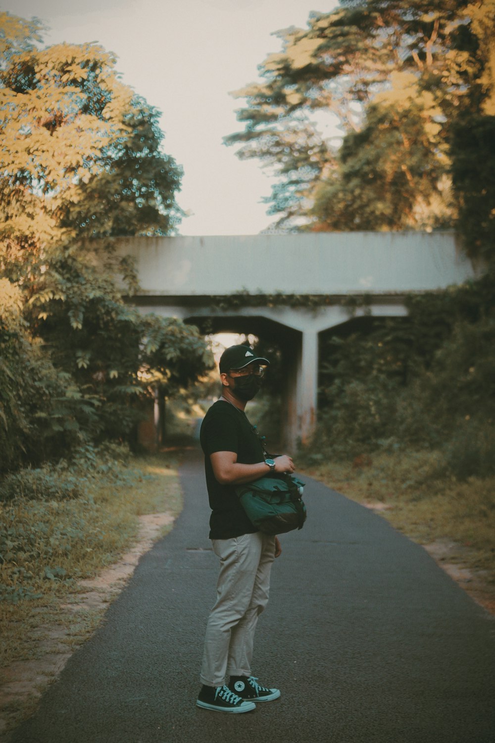 man in black t-shirt and gray pants carrying black backpack walking on pathway during daytime