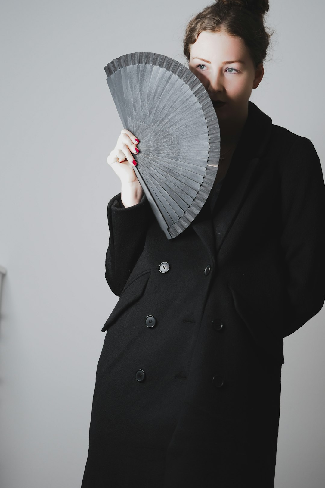 person in black coat holding gray hand fan