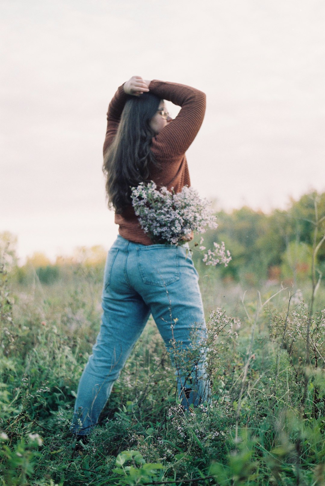 woman in brown long sleeve shirt and blue denim jeans standing on green grass field during