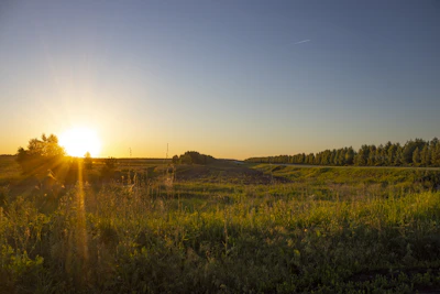 A serene sunset casting warm light over a quiet, open land area.