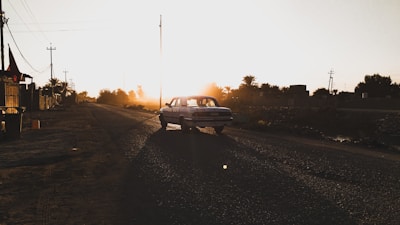 A scenic shot of a classic car cruising along a winding country road at sunset.