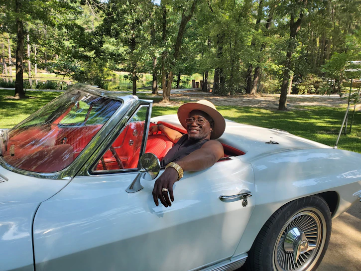 A happy car owner taking photos of their vehicle in a sunny driveway, preparing to list it online.