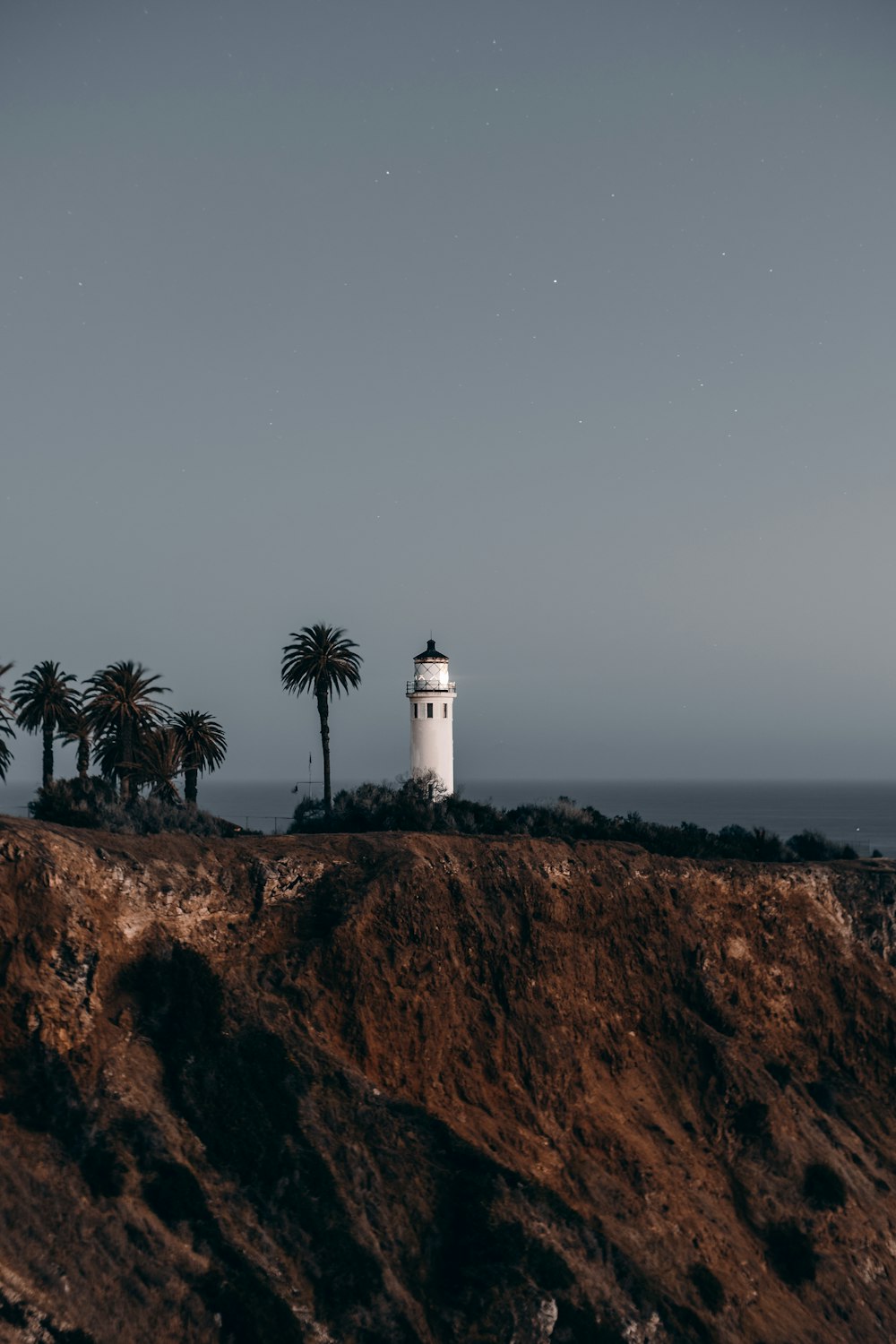 white lighthouse on brown rocky hill under gray sky