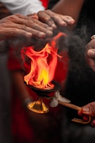 Close-up of hands holding a traditional brass lamp with flickering flames during the Ganga Aarti ceremony.