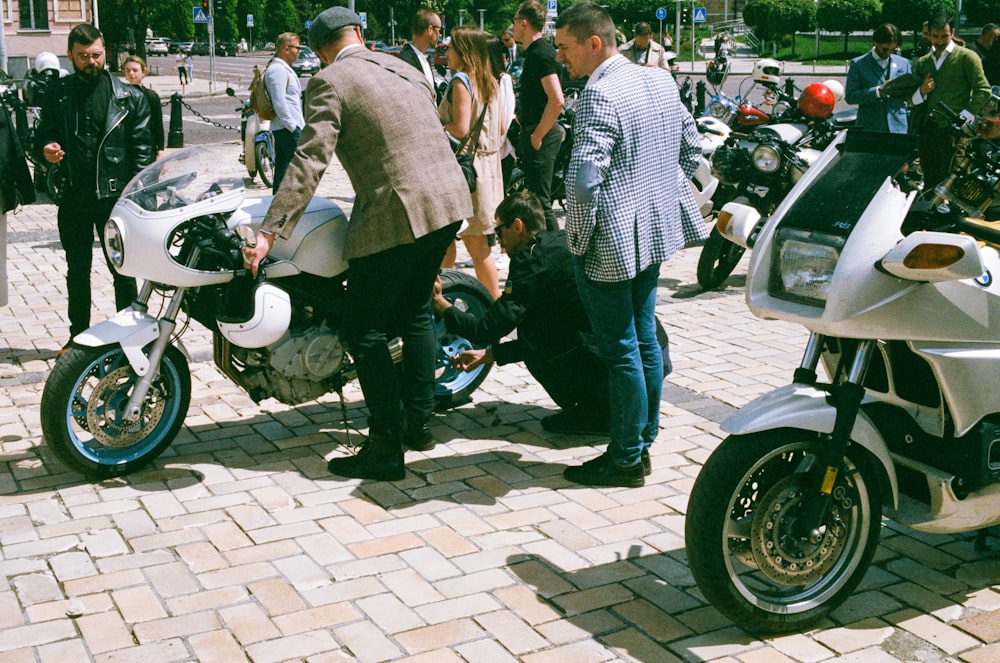 man in gray suit jacket and blue denim jeans standing beside black motorcycle during daytime