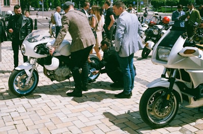 man in gray suit jacket and blue denim jeans standing beside black motorcycle during daytime distinguished google meet background