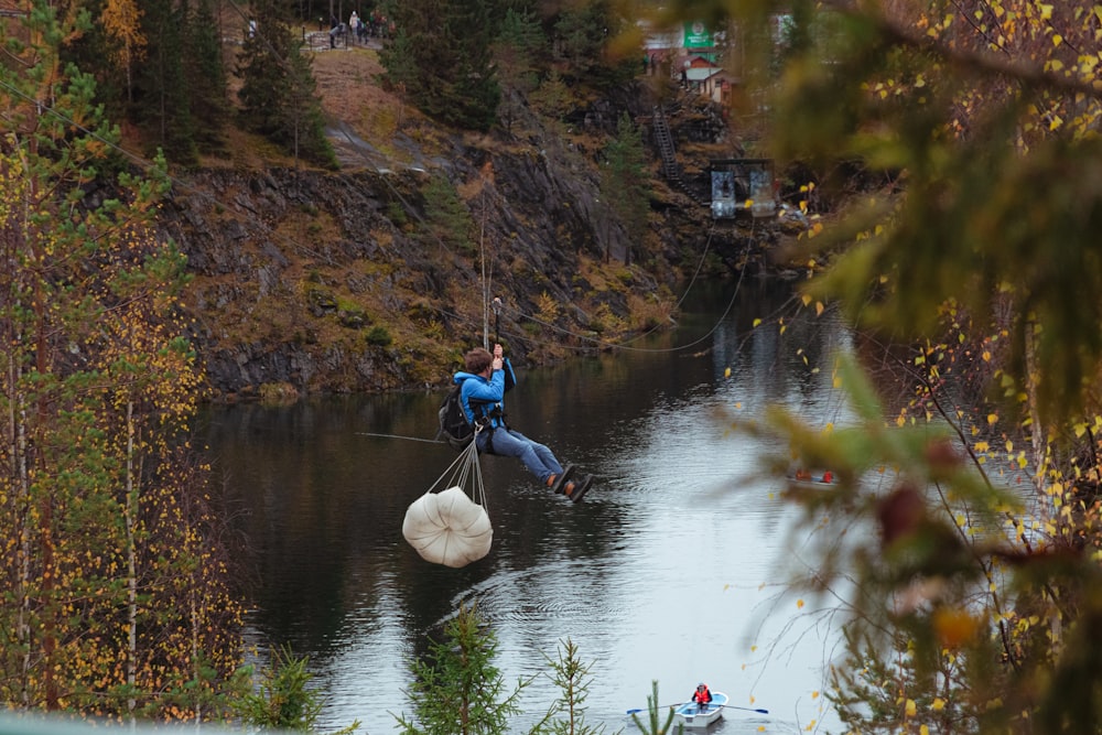 Mann in blauer Jacke und blauer Jeans sitzt tagsüber auf weißem Felsen im Fluss