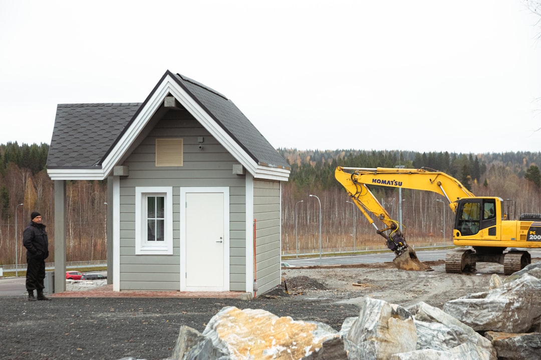 white and blue wooden house near yellow and black excavator during daytime