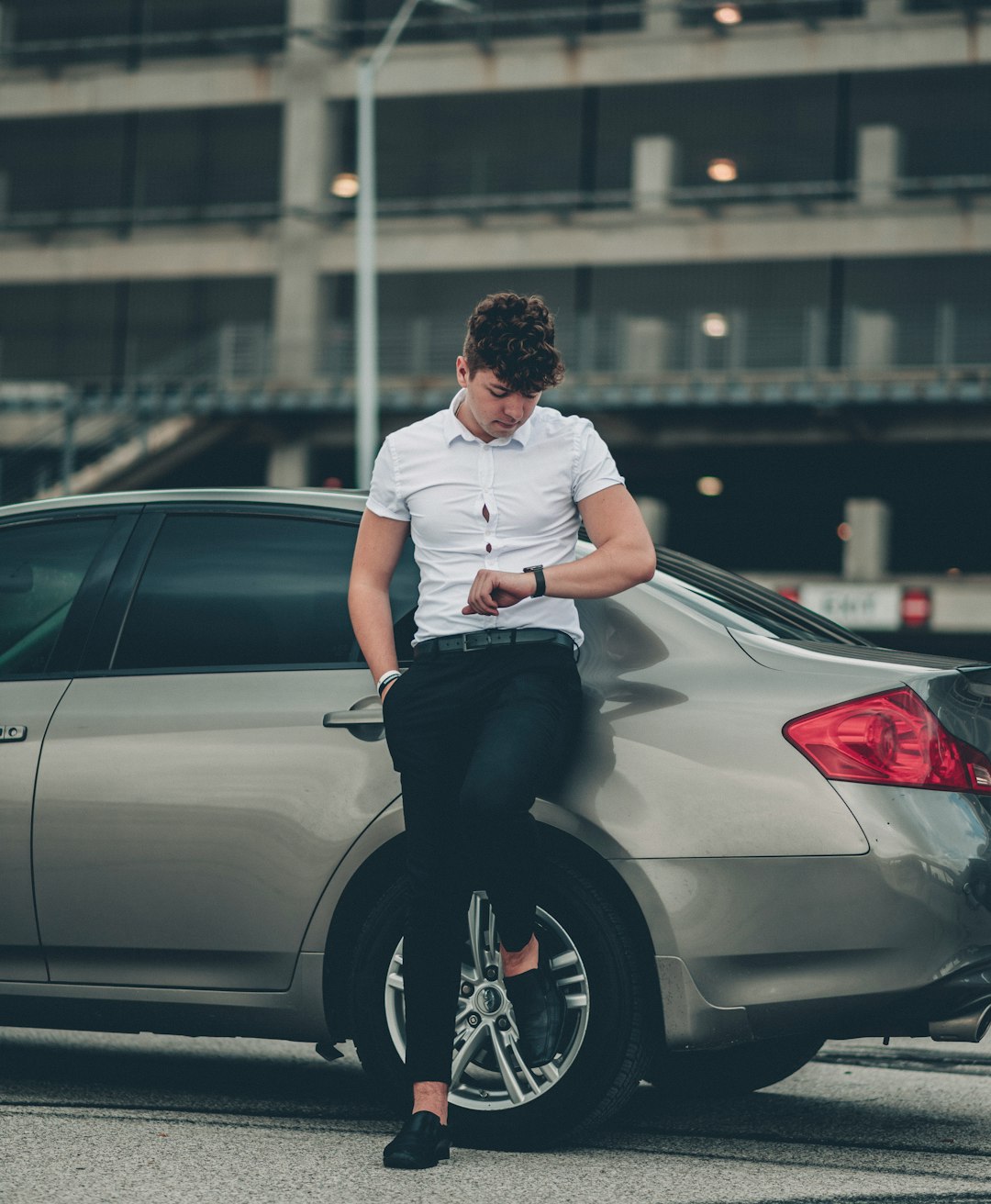 man in white t-shirt and black pants sitting on silver car