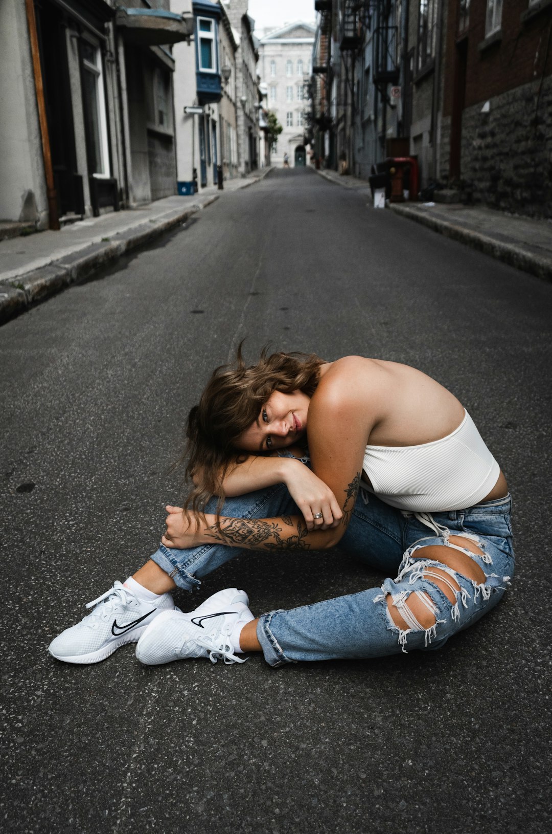 woman in white tank top and blue denim jeans lying on road during daytime