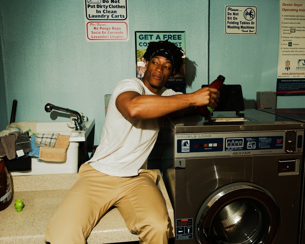 man in white t-shirt and beige pants sitting on front load washing machine