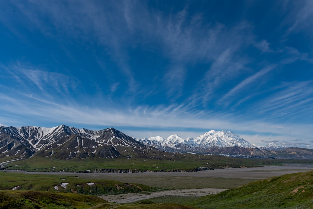 green grass field near snow covered mountain under blue sky during daytime