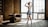 A dancer is poised elegantly in a well-lit room with large grid windows and a rustic vibe. The wooden floors and exposed brick walls add to the vintage atmosphere. An antique leather chair and a globe are visible in the background.