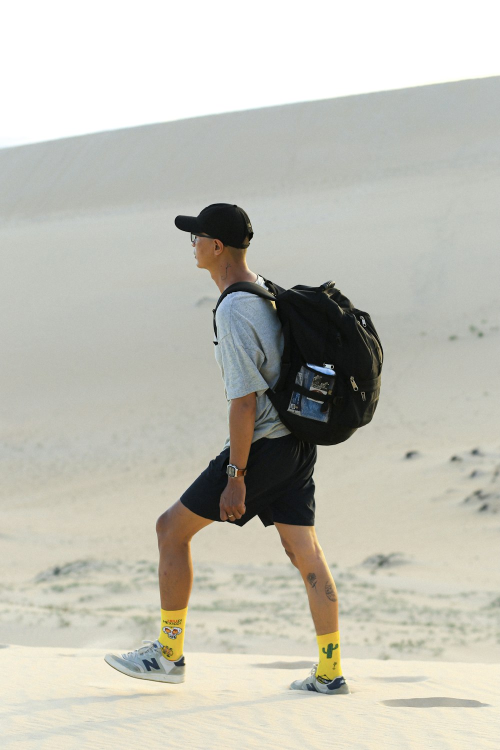 hombre con camiseta blanca y pantalones cortos negros con mochila negra caminando sobre arena blanca durante